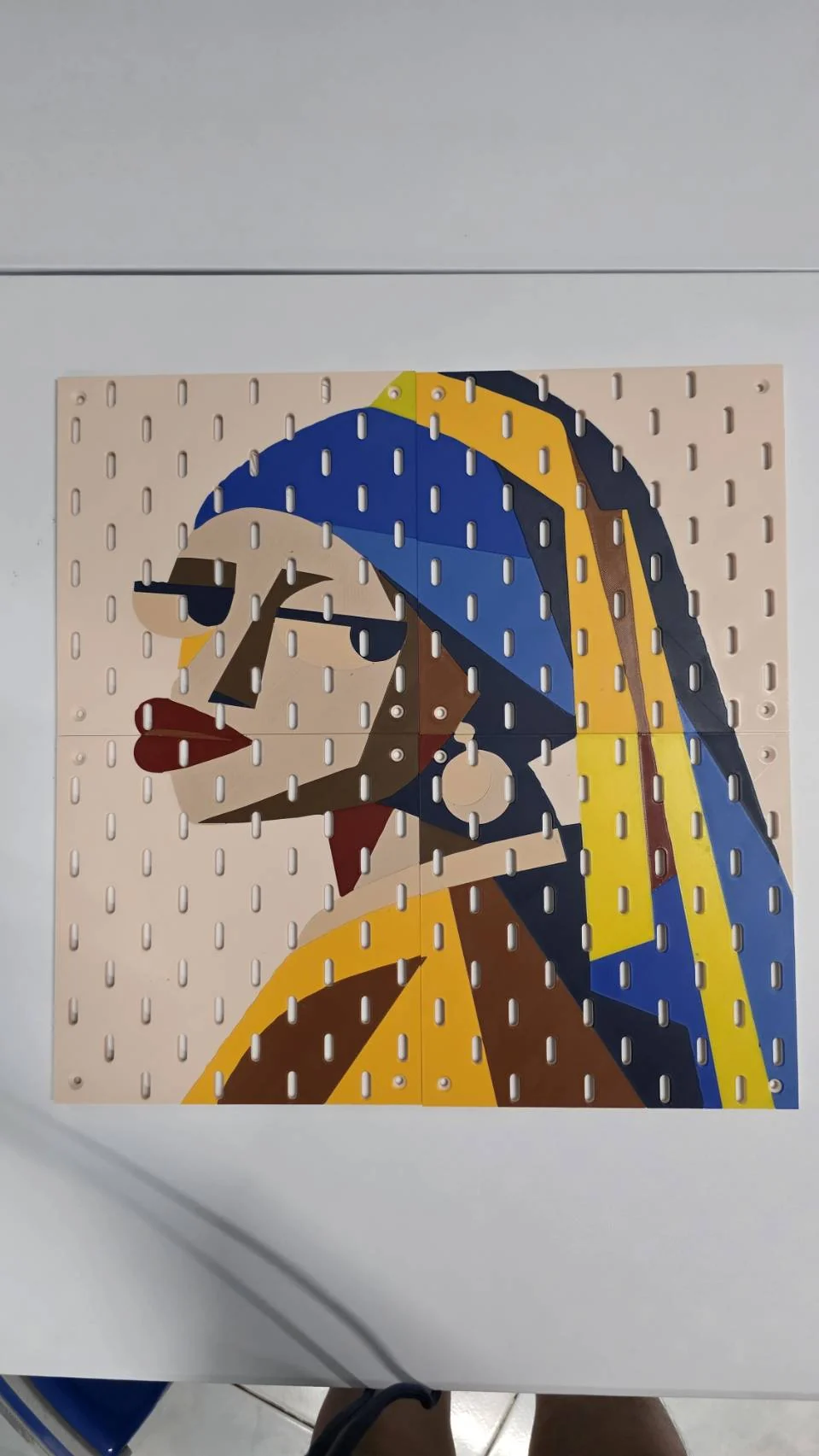 Four printed pegboard panels form a geometric girl with a blue headscarf and yellow accents